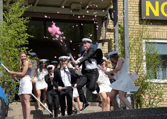 Studenter som kommer ut vid Nolaskolan. En student skjuter ut konfetti i rosa färger. Foto.