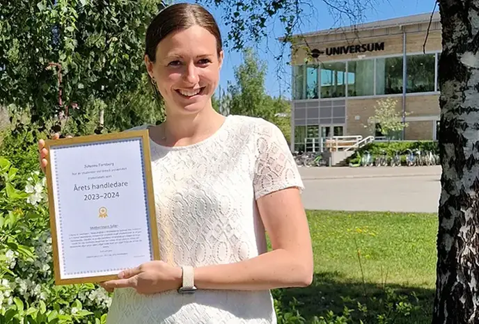 Johanna Forsberg visar upp diplomet för Årets handledare stående ute i en grönskande park.