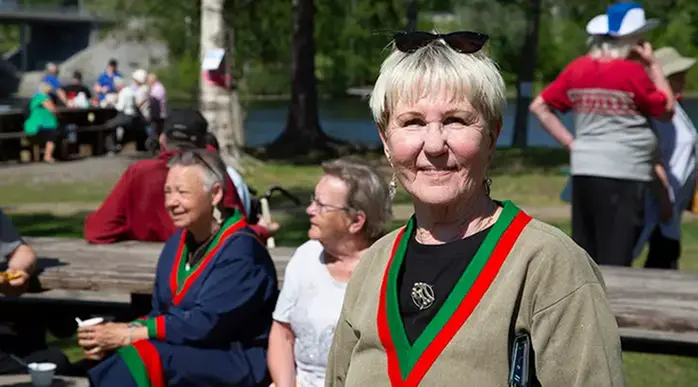 Kvinna i samisk dräkt, i bakgrunden siter två kvinnor och samtalar vid ett bord