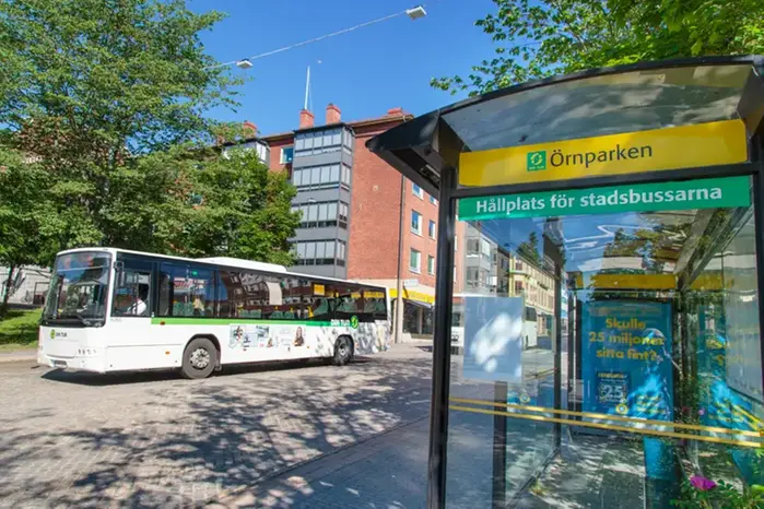 Solig dag och en buss passerar förbi en hållplats i vad som ser ut att vara centralt i en stad. 